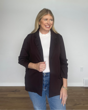 Load image into Gallery viewer, Woman wearing a brown blazer over a white shirt and blue jeans in a room with a white wall and wooden floor.
