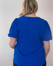 Load image into Gallery viewer, Back of woman wearing a short sleeve royal blue shirt with puff sleeves.