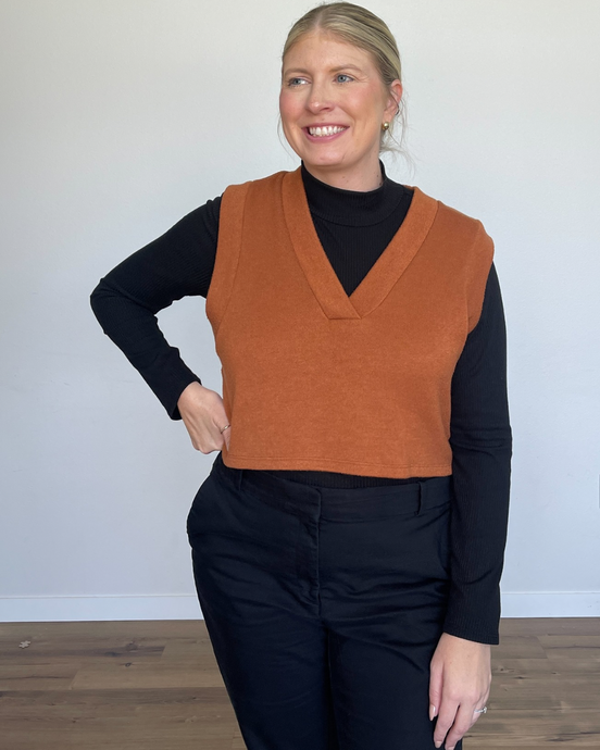 Woman wearing a camel colored cropped sweater vest with a black long sleeve turtleneck underneath