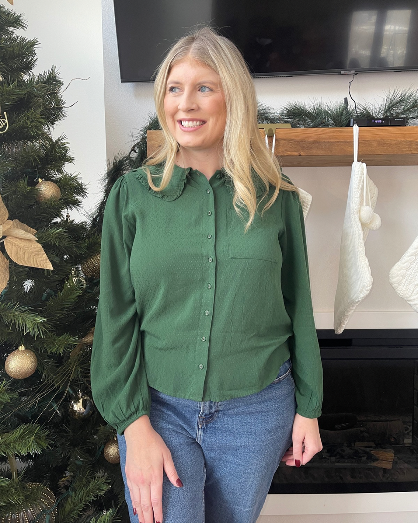 Woman wearing a green blouse and blue jeans standing in front of a decorated Christmas tree.