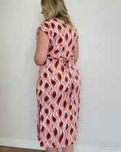 Load image into Gallery viewer, Woman wearing a rust, mauve and white patterned dress against a white wall
