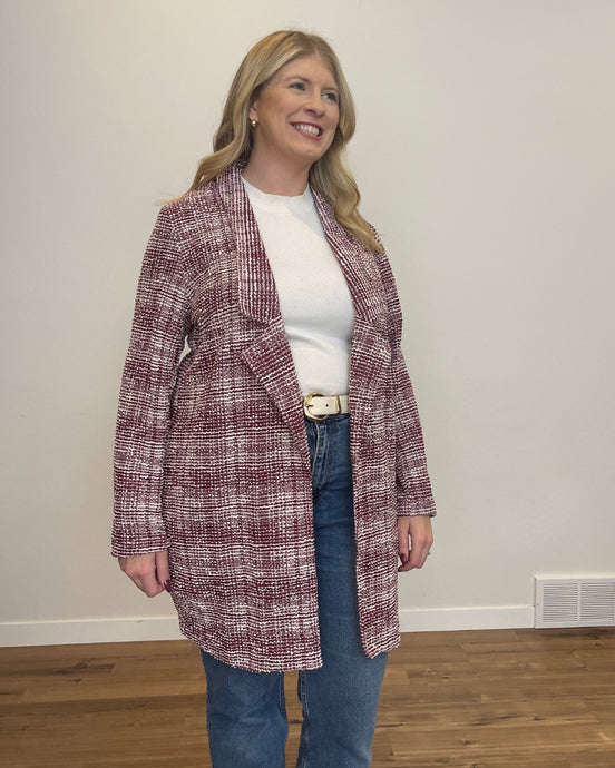 Woman wearing a textured maroon and ivory long blazer over a white shirt and blue jeans.