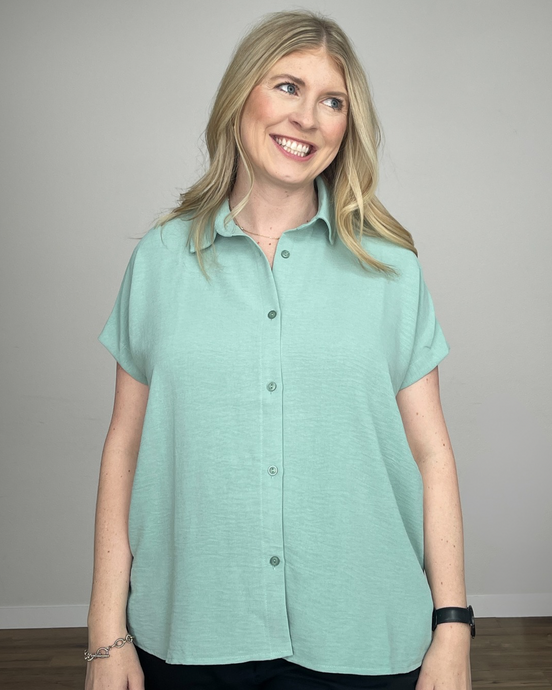 Woman wearing a short sleeve seafoam green button up shirt.