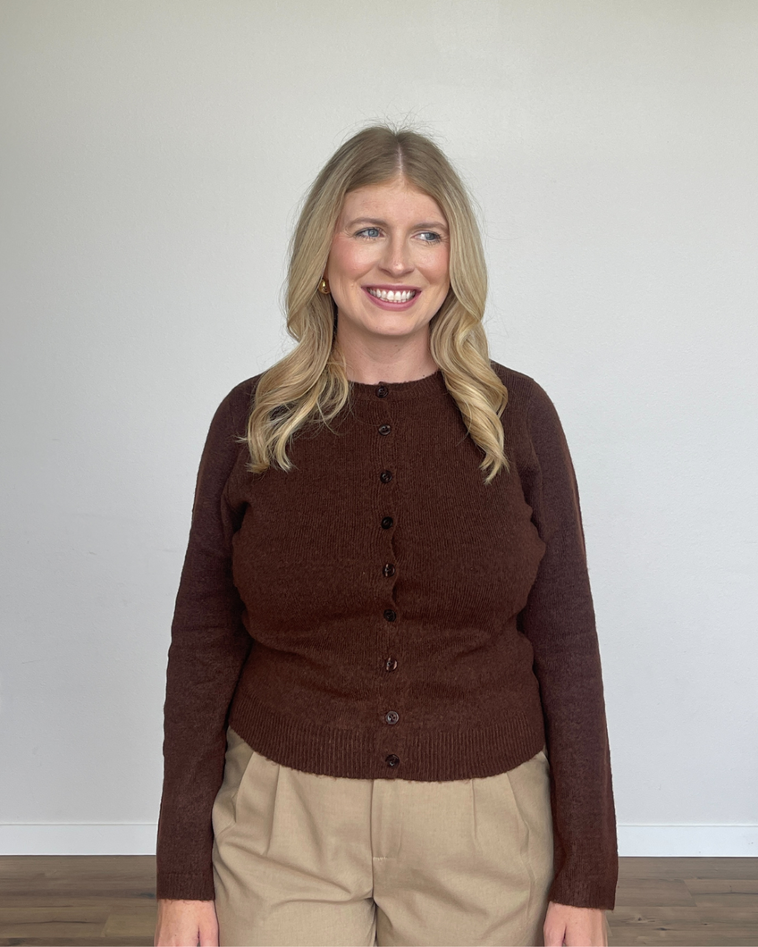 Woman wearing a brown sweater and beige pants against a plain background