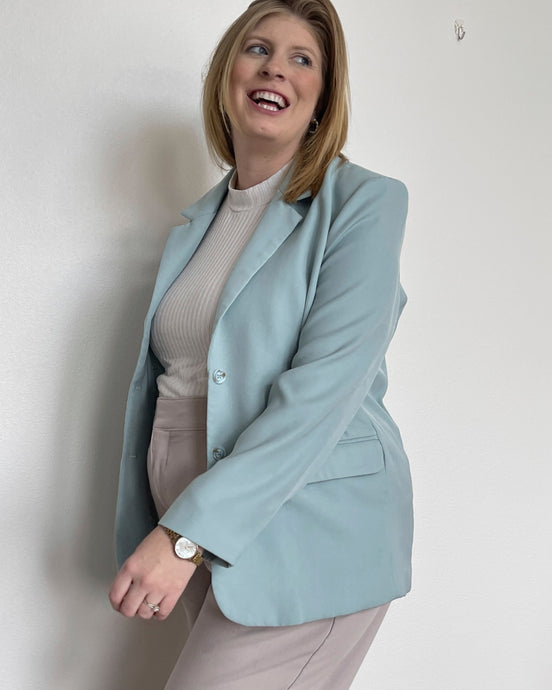 Woman wearing a light blue, long sleeve solid woven blazer with an open front featuring functional buttons and pockets